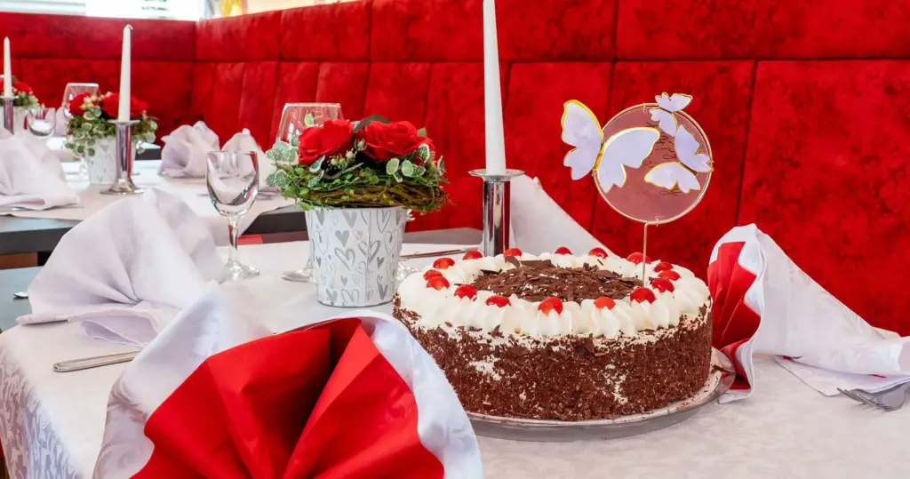 Restaurant Roma – Aufnahme des Innenraumes mit roten Sitzbänken, weiß-roten Tischgarnituren und einer frischen Schwarzwälder-Kirsch-Torte